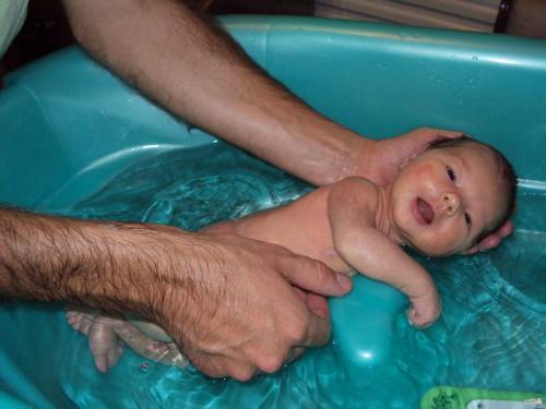 Новорожденного купают в ванночке